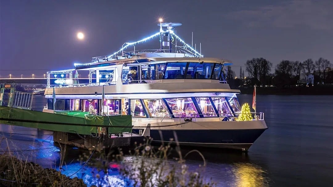 Festively lit boat on the Rhine River during Cologne Advent tour with moonlit sky.