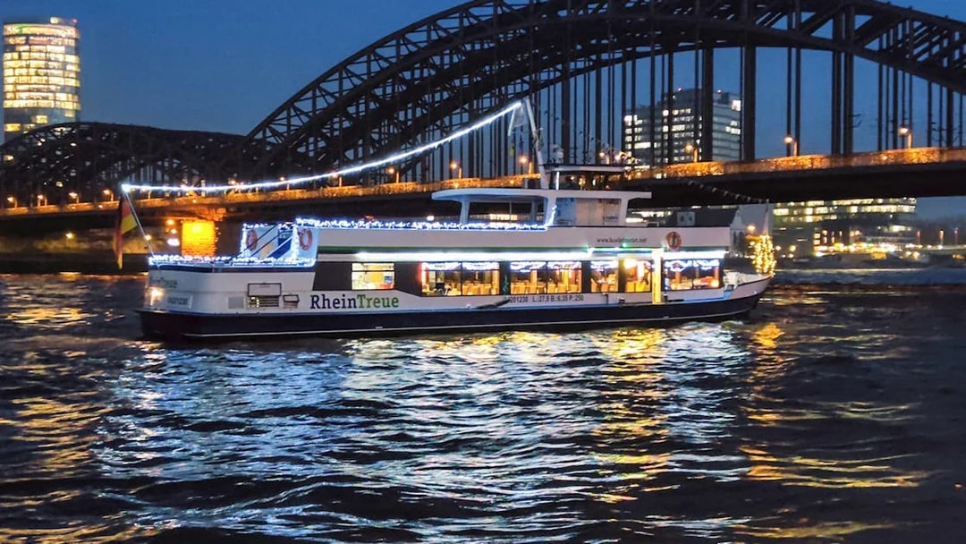 Cologne river cruise boat with festive lights near Hohenzollern Bridge at night.