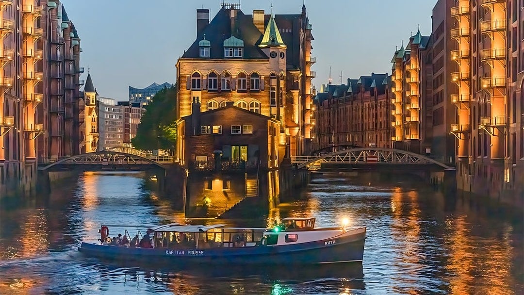 Evening cruise boat on illuminated canal in Hamburg's Speicherstadt district.