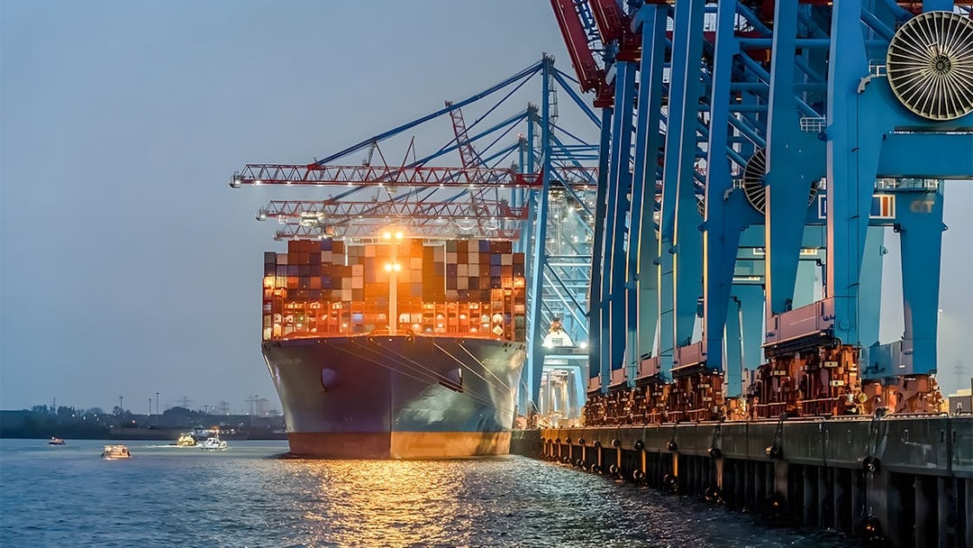 Container ship docked at illuminated harbor cranes during evening Grand Harbor cruise.