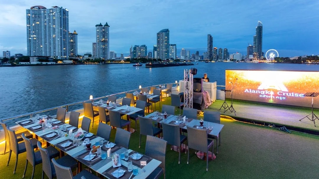 Dinner setup on a cruise ship deck with Chao Phraya River and Bangkok skyline in the background.