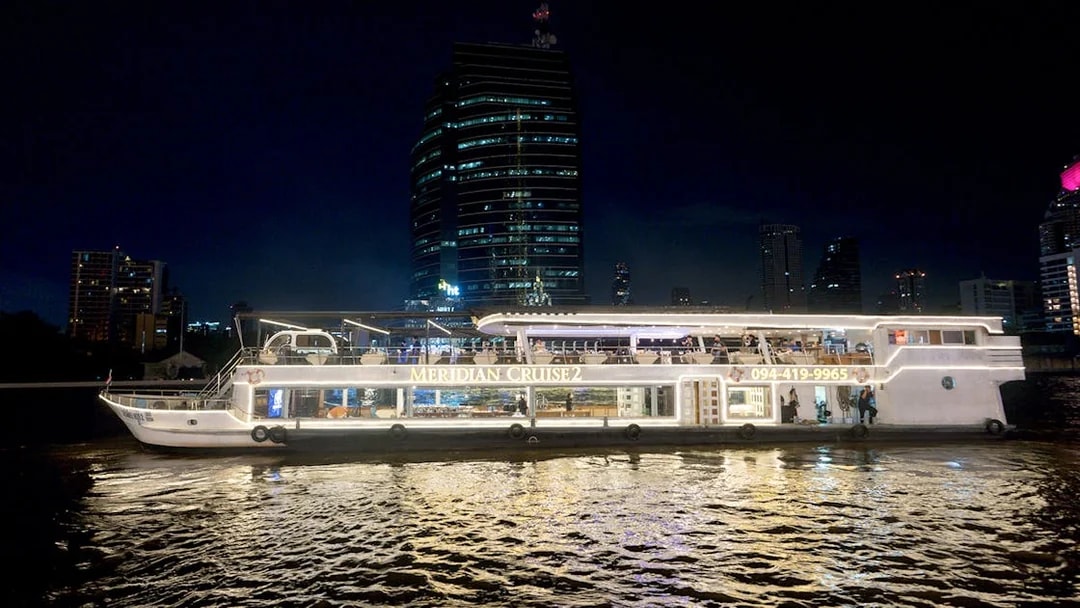 Meridian Cruise boat on Chao Phraya River at night, Bangkok skyline in background.