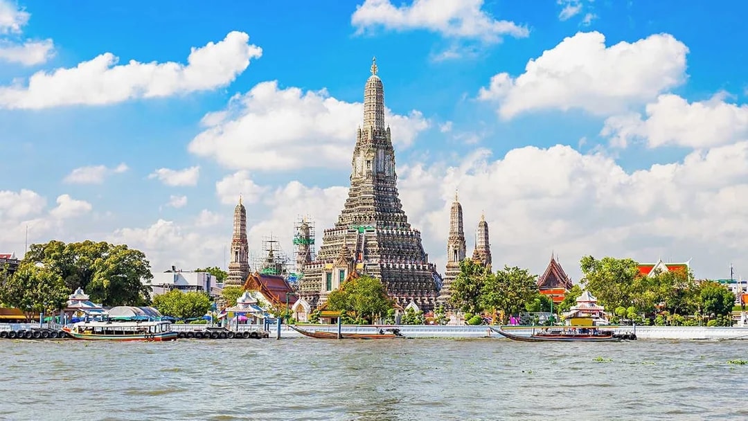 Wat Arun temple on Chao Phraya River, Bangkok, with boats in foreground.