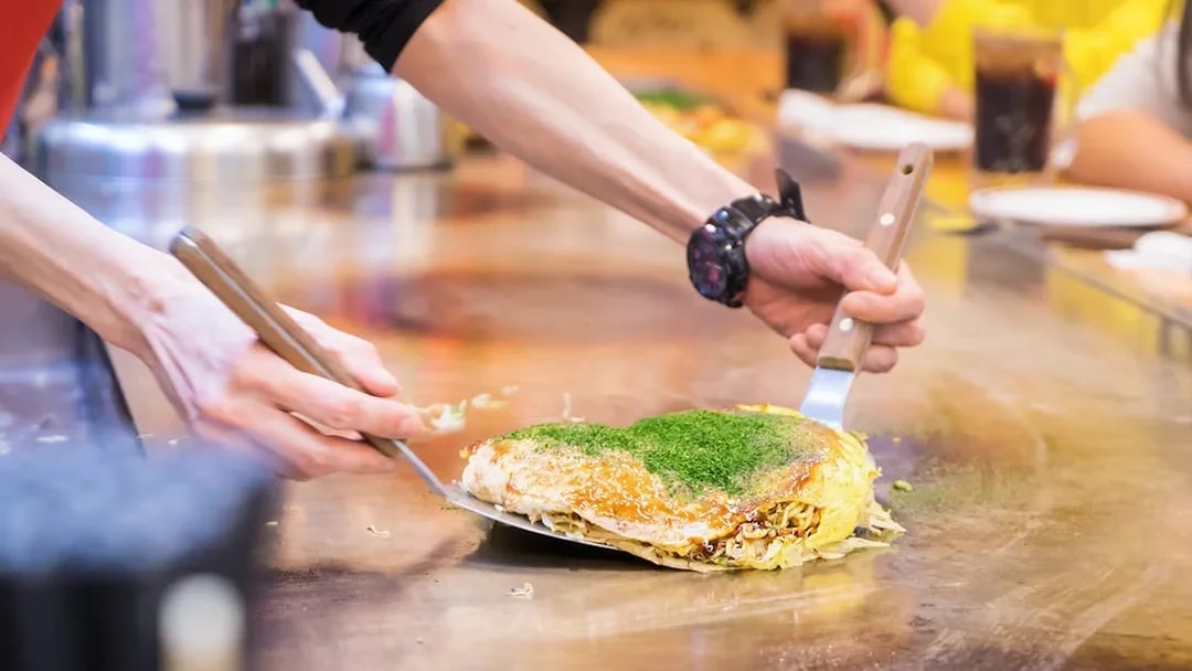 Chef preparing okonomiyaki on a hot griddle in Japan.