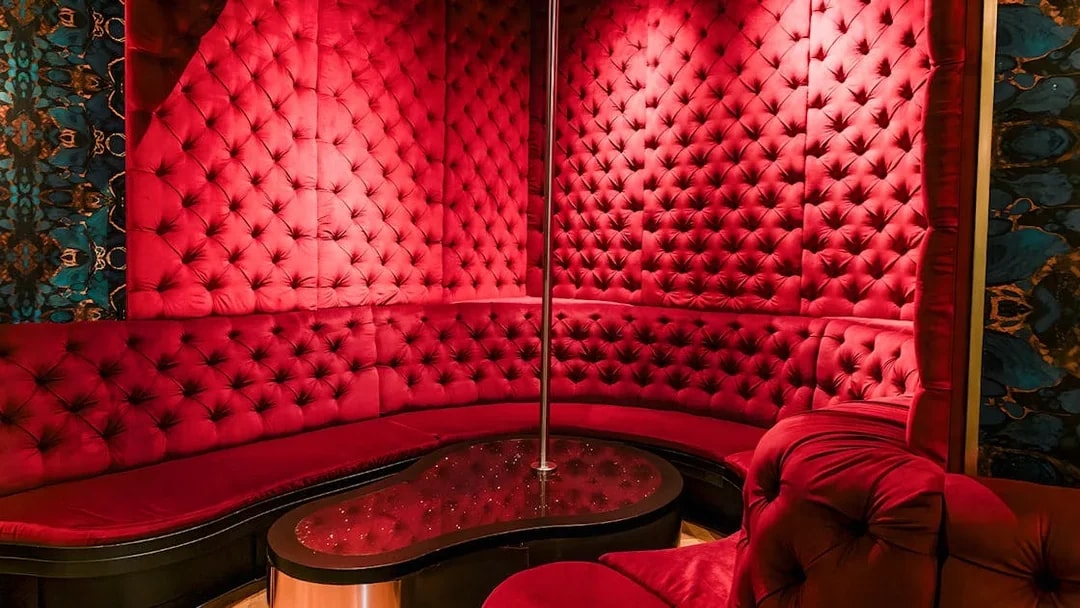 Luxurious red velvet seating area with a pole at Tour de BonTon strip club.