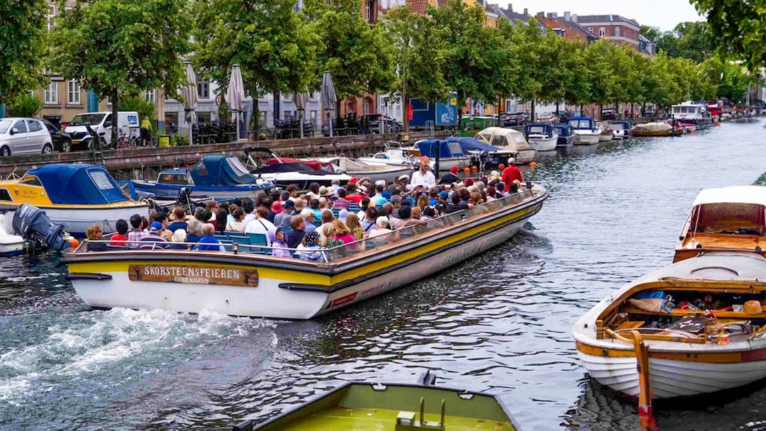 People enjoying a canal cruise in Copenhagen, passing by moored boats and tree-lined streets.