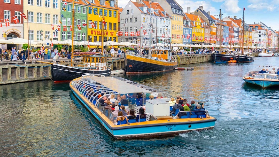 Canal tour boat in Nyhavn, Copenhagen, passing colorful buildings and docked ships.