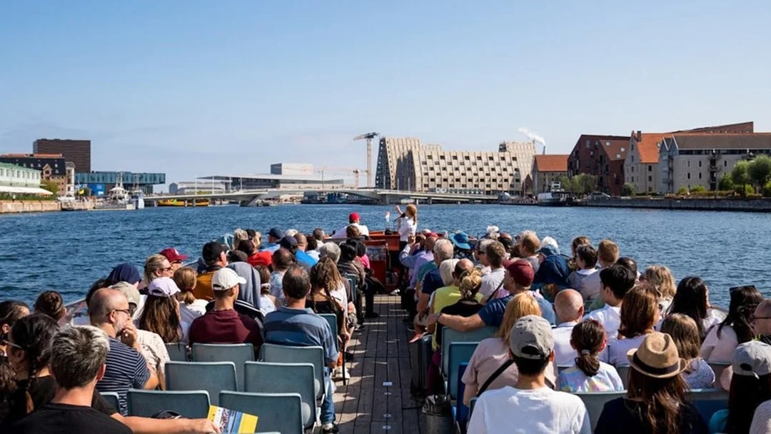 Tourists on a boat tour in Copenhagen, viewing waterfront architecture and landmarks.