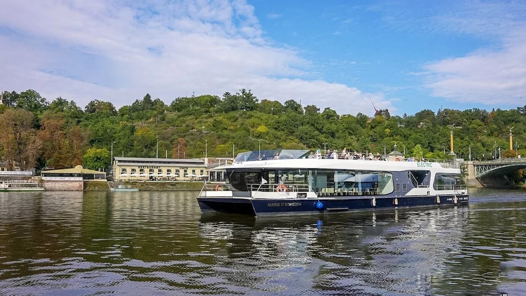 Cruise boat on Vltava River with passengers enjoying scenic views of Prague.
