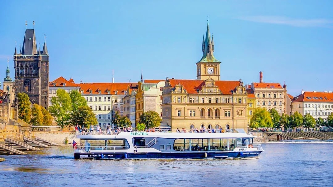 Electric boat cruising on Vltava River with Prague's historic buildings in the background.