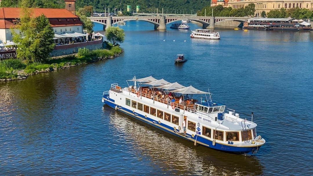 Vltava River cruise boat near Prague's historic bridges and riverside buildings.