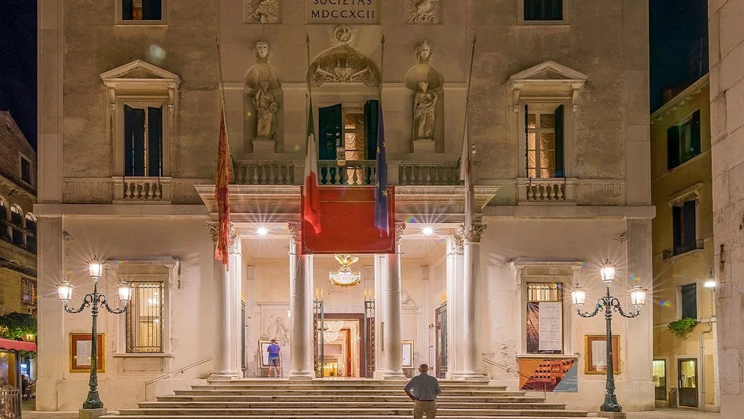 Facade of Fenice Theater in Venice at night, featuring illuminated entrance and architectural details.