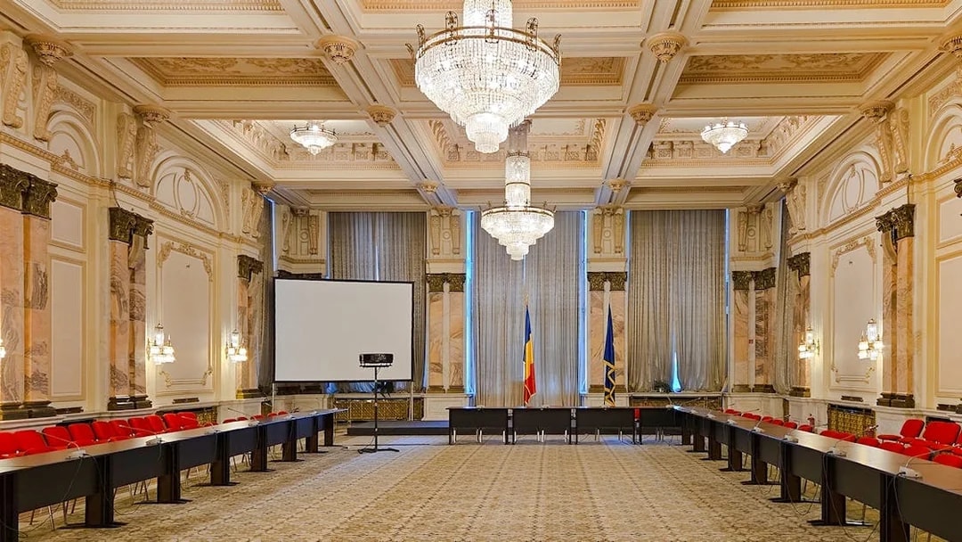 Palace of Parliament conference room with chandeliers and Romanian flags.
