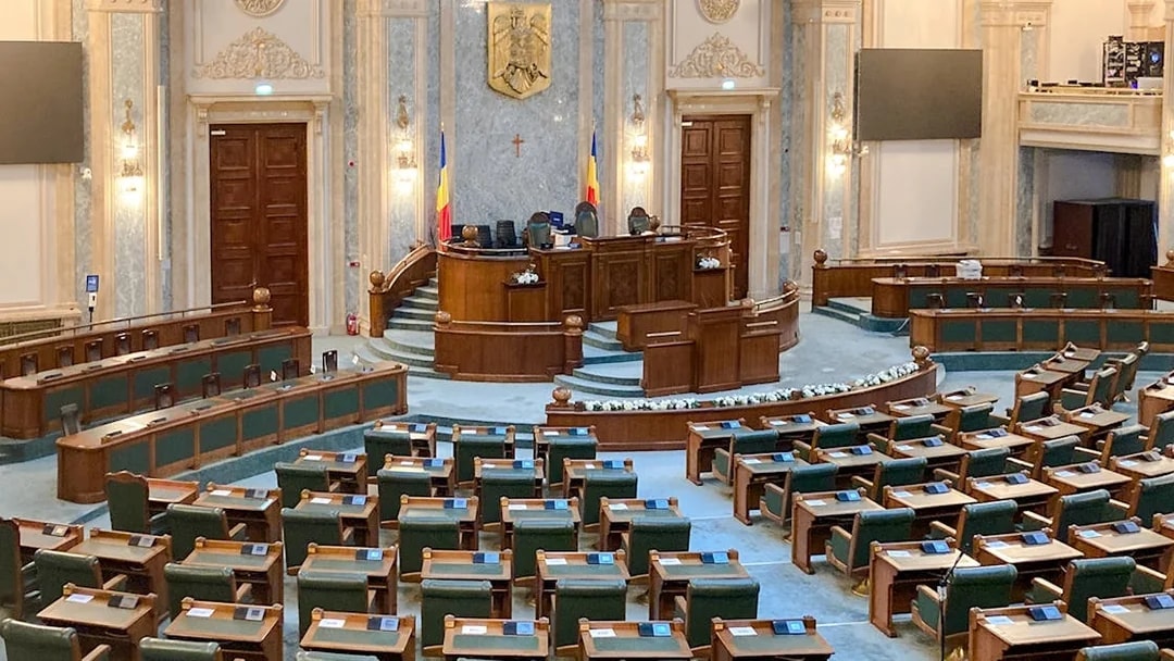 Parliament chamber with wooden desks and Romanian flags inside Palace of Parliament.