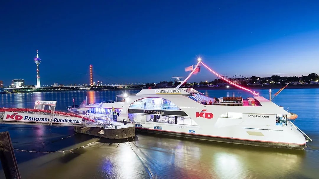 Cruise ship docked on the Rhine River in Düsseldorf with city skyline and Rheinturm Tower.