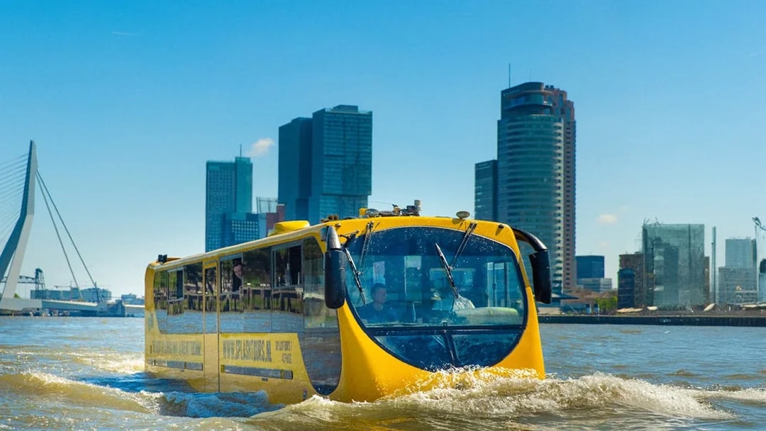 Amphibious bus on Rotterdam waterway with city skyline in background.
