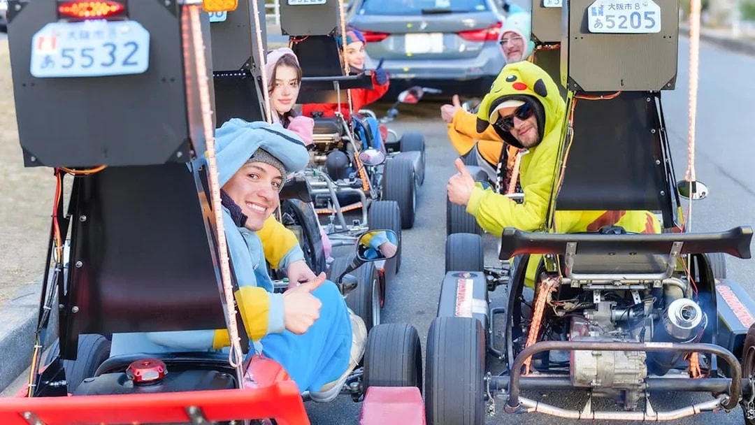 Friends in costumes sitting in go-karts, Osaka street tour.