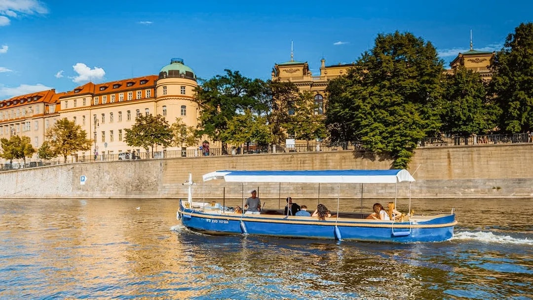 Sightseeing cruise boat on Devils Channel in Prague with historic buildings in the background.