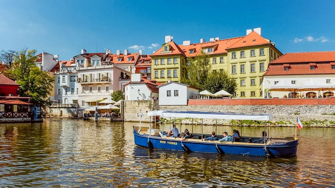 Sightseeing cruise boat on Devils Channel with colorful buildings in Prague.