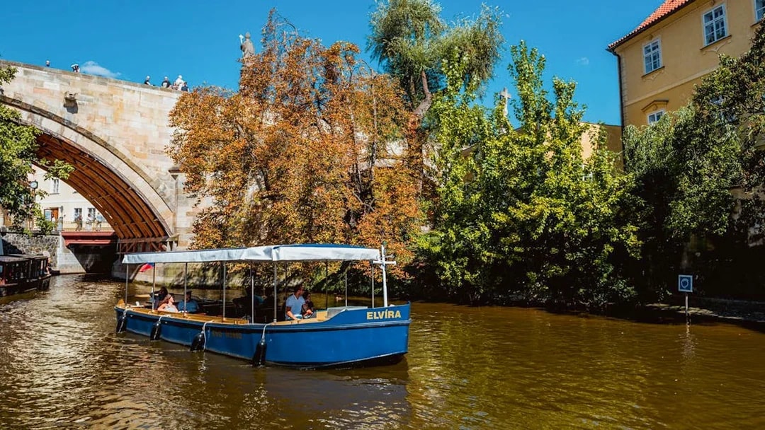 Sightseeing cruise boat on Devils Channel in Prague passing under a stone bridge.