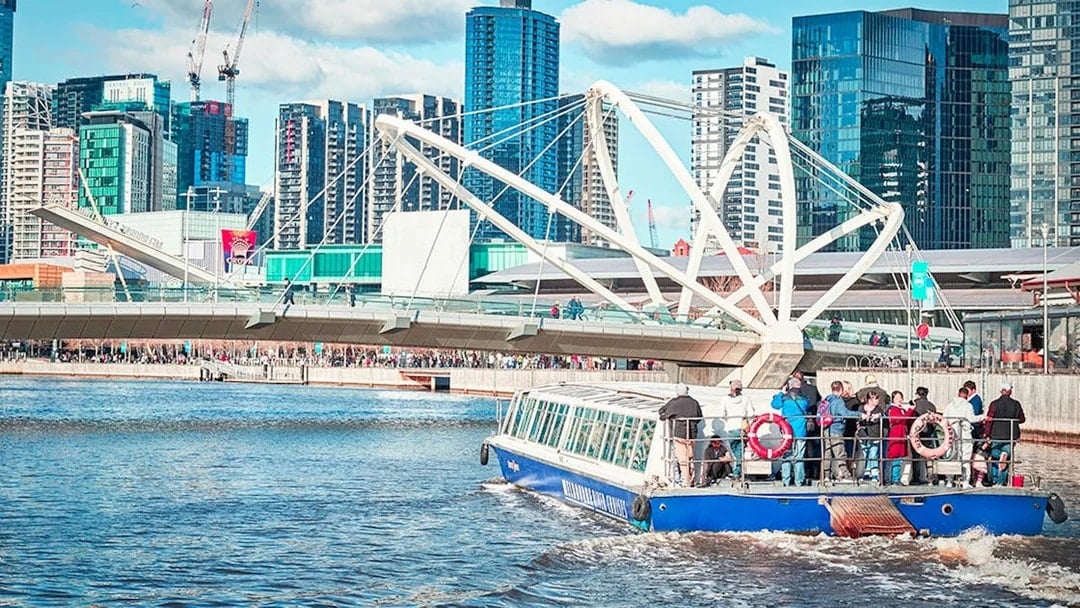 Tourists on a river cruise boat passing under a modern bridge in a cityscape.