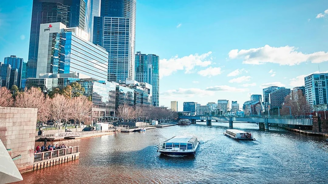 City river cruise with boats passing modern skyscrapers and a bridge in Melbourne.