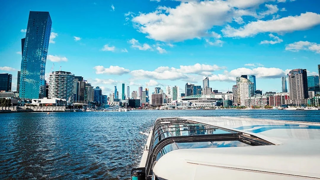 Cruise boat on river with city skyline and modern buildings in the background.