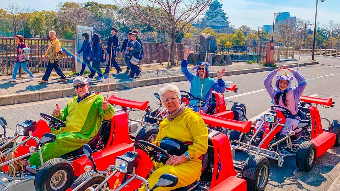 Go-kart riders in costumes on Osaka street with Osaka Castle in the background.