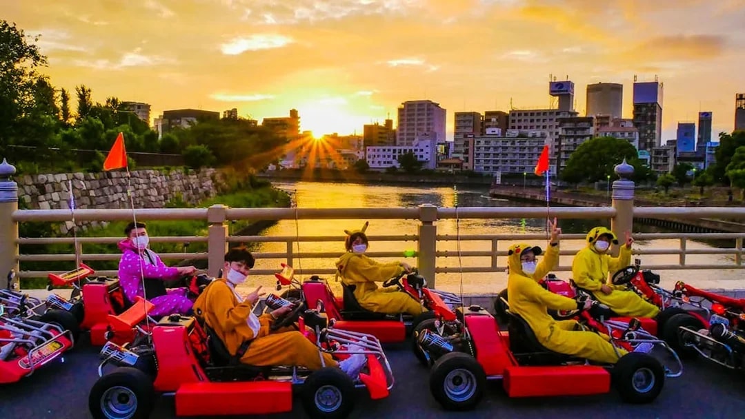 Go-kart riders in costumes on a bridge during sunset, Akiba Kart Osaka Street Go Kart Experience.