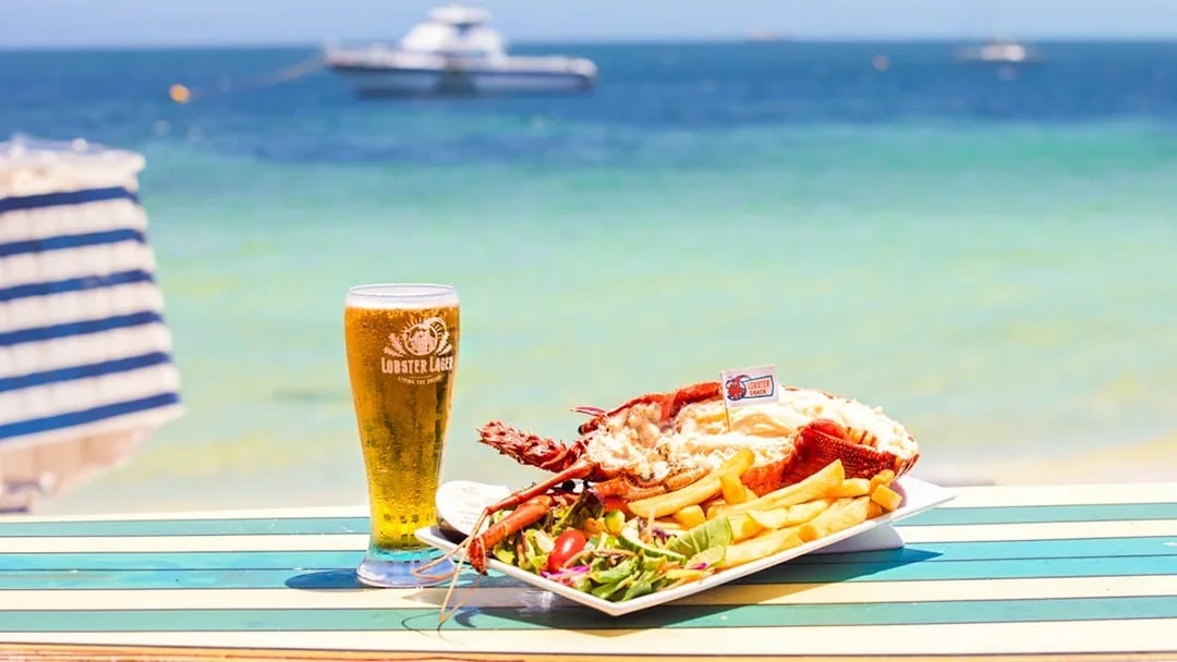 Lobster meal with fries and salad on a beachside table in Australia, with a glass of beer.