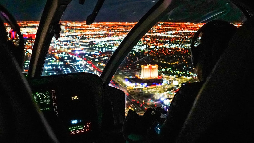 Helicopter cockpit view over city lights at night.