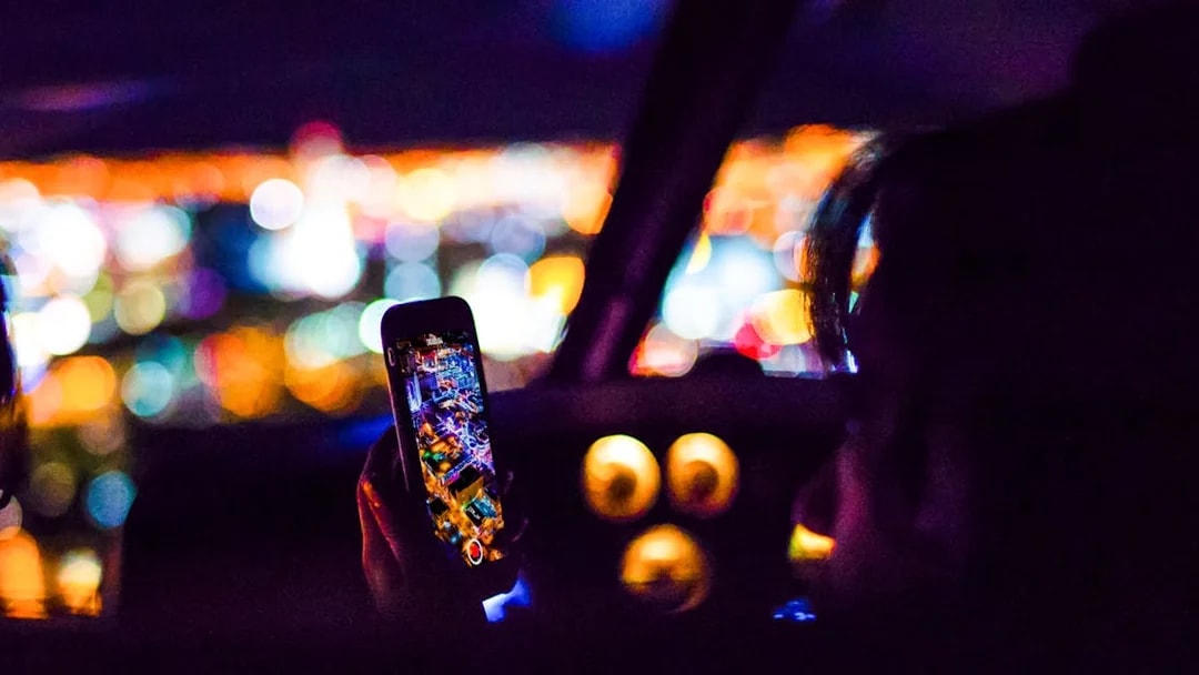 Person photographing city lights from helicopter cockpit at night.