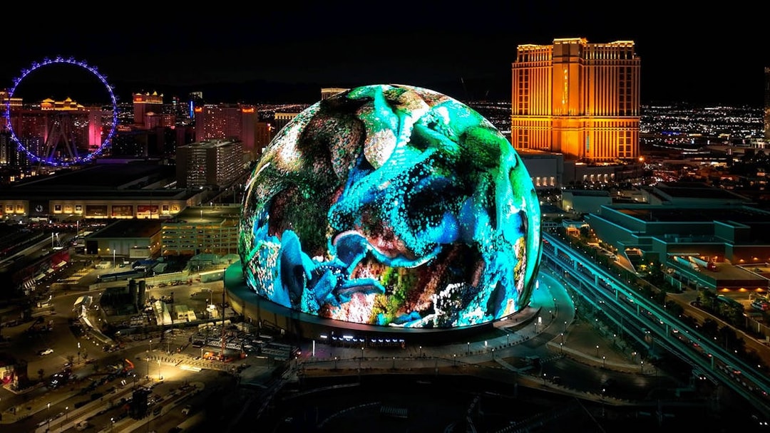 Las Vegas Sphere illuminated at night with vibrant display, Nevada skyline in background.