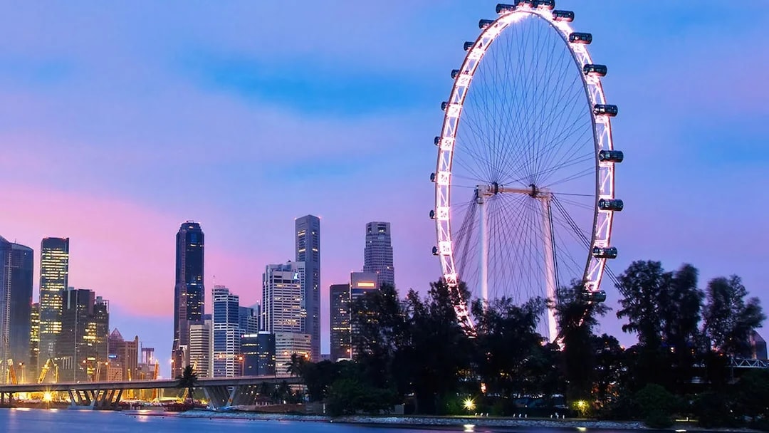 Singapore Flyer illuminated at dusk with city skyline in the background.