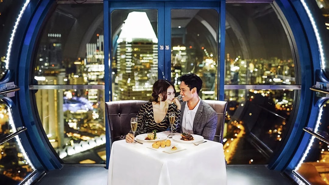 Couple dining in a Singapore Flyer capsule with city skyline view.
