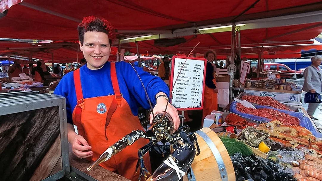 Bergen fish market vendor holding lobster, showcasing seafood selection.