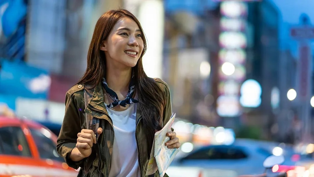 Person holding a map, smiling on a street in Osaka Namba, Japan.