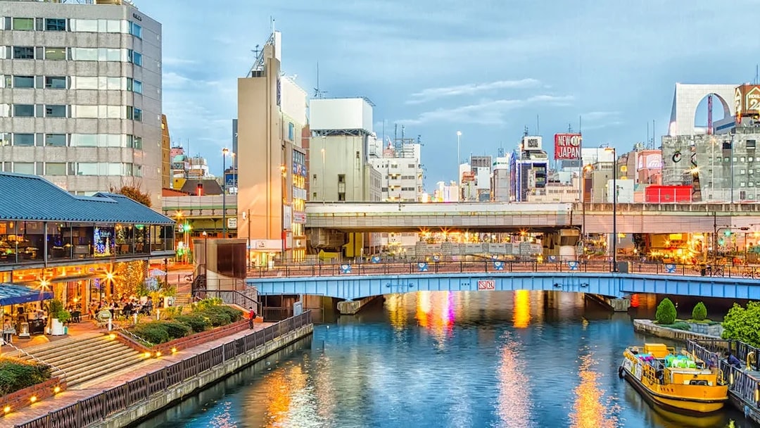 Dotonbori canal with illuminated buildings and a yellow boat in Osaka, Japan.