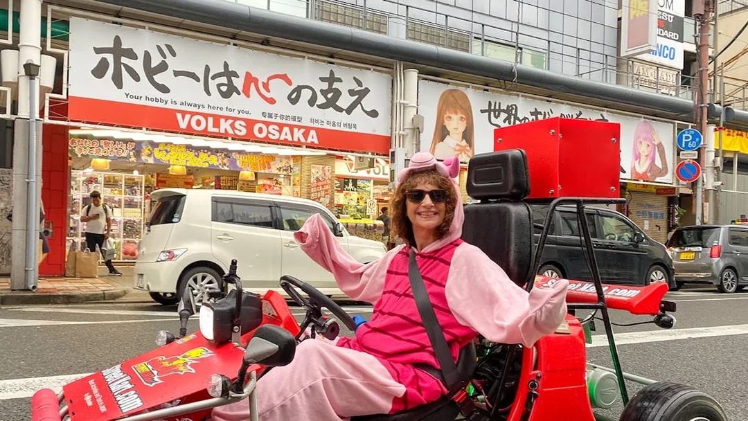 Person in costume driving a go-kart on Osaka Namba street.