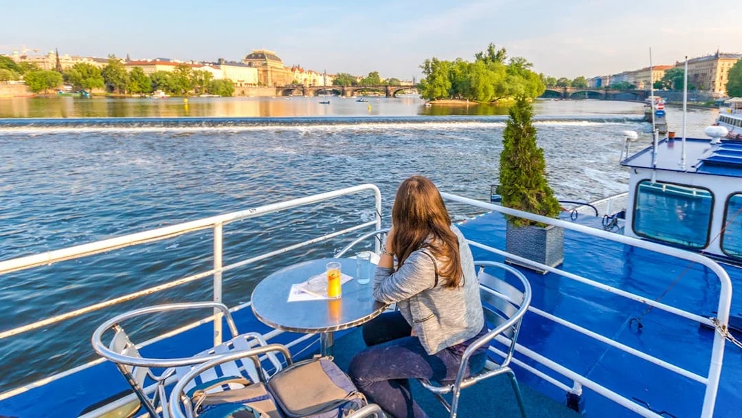 Person enjoying Vltava River view from a cruise deck in Prague.