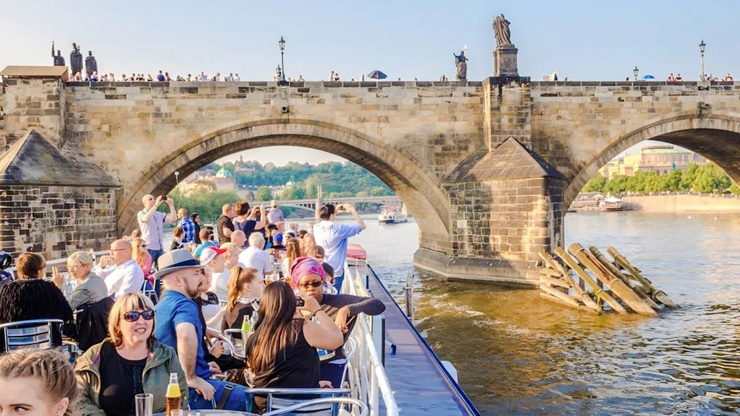 Sightseeing cruise under Charles Bridge in Prague with tourists on deck.