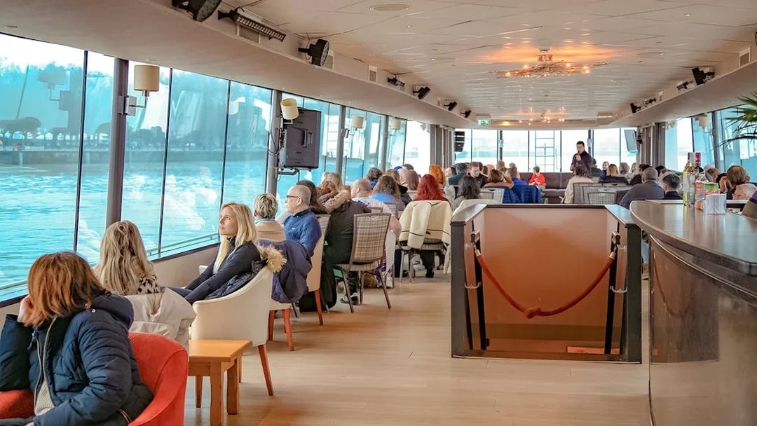 People enjoying a scenic Bordeaux river cruise inside a boat with large windows.