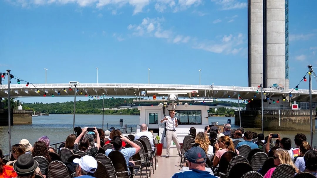 Guide giving live commentary on Bordeaux river cruise with bridge in background.