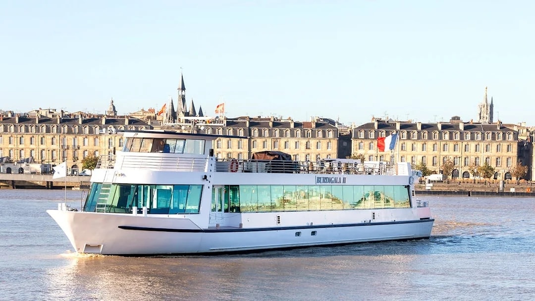 River cruise boat on the Garonne with Bordeaux cityscape in the background.