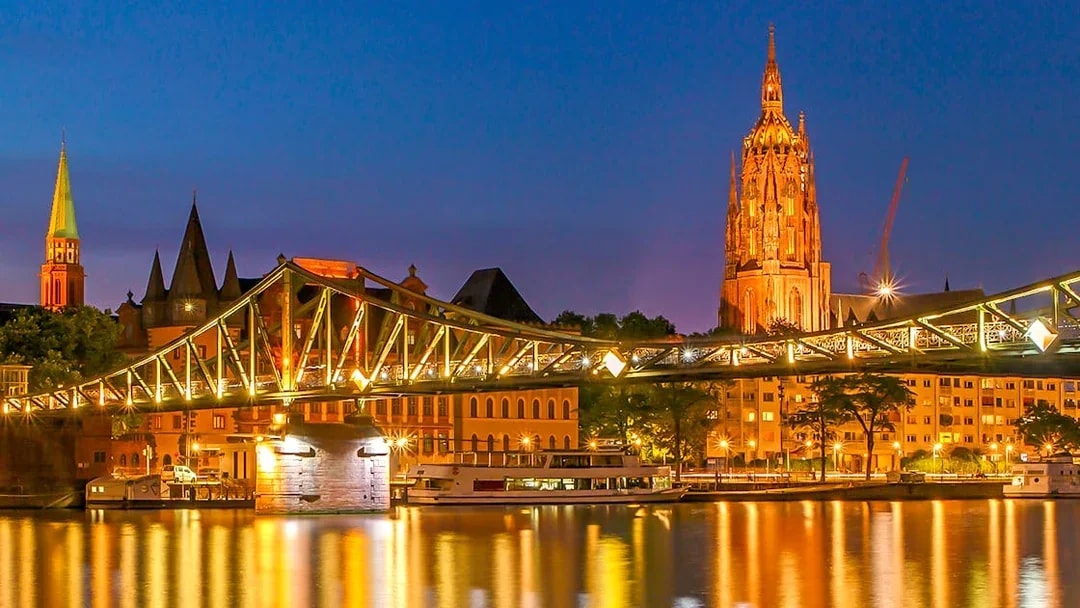 Frankfurt Cathedral and illuminated bridge during evening cruise.