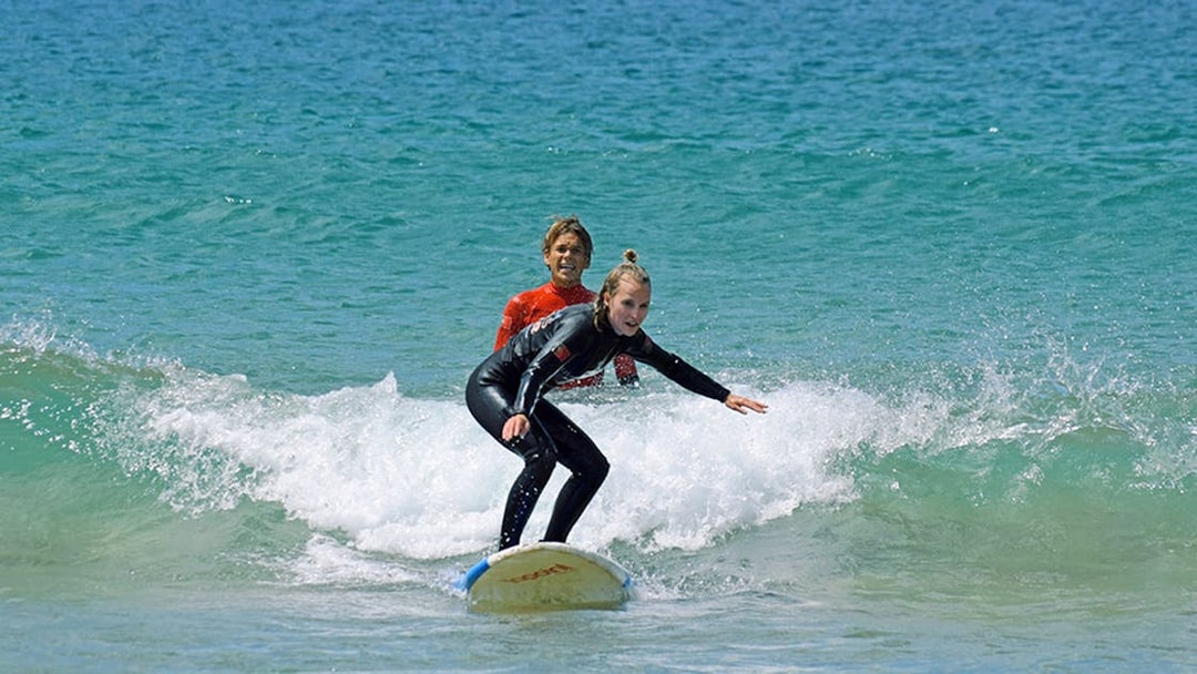 Group surf lesson with instructor guiding a student on a wave.