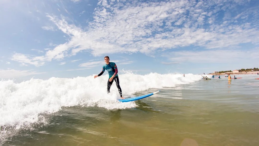 Group surf lesson with participants riding waves at a beach.