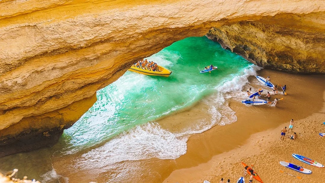 Boat tour entering Benagil Caves with people kayaking and paddleboarding on the beach.
