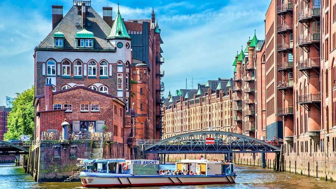 Harbor cruise boat passing historic brick buildings in Hamburg's Speicherstadt district.