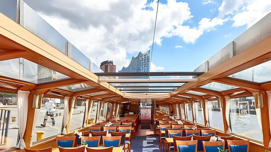 Interior of a tour boat with seating, Elbphilharmonie visible through windows, Hamburg Harbor Cruise.